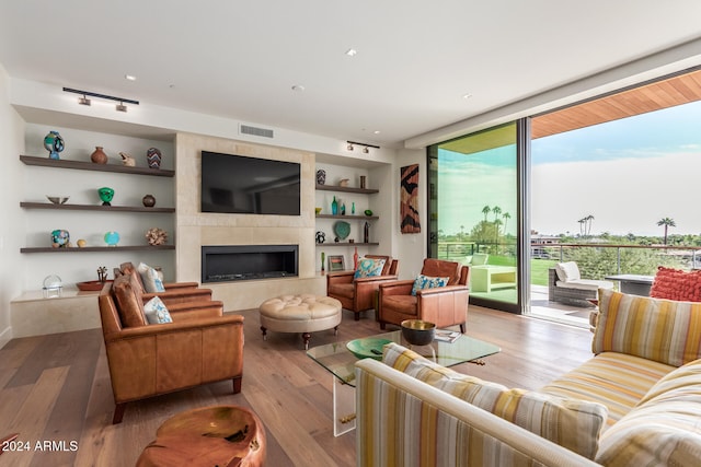 living room featuring a tile fireplace, built in shelves, and light hardwood / wood-style flooring