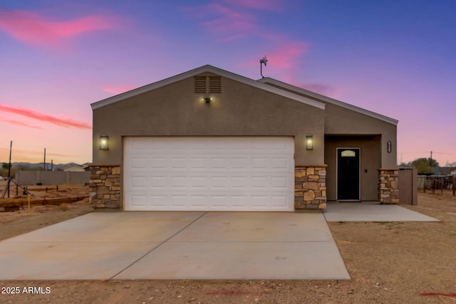 view of front of home with stone siding, an attached garage, concrete driveway, and stucco siding