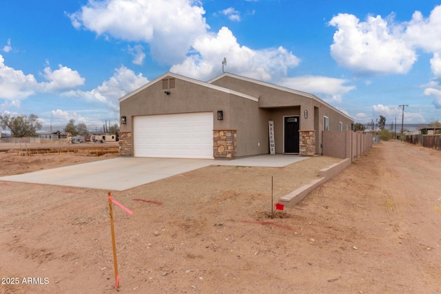 view of front of home featuring stucco siding, concrete driveway, an attached garage, fence, and stone siding