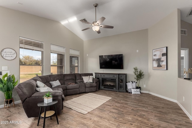 living room featuring a fireplace, visible vents, ceiling fan, vaulted ceiling, and wood finished floors