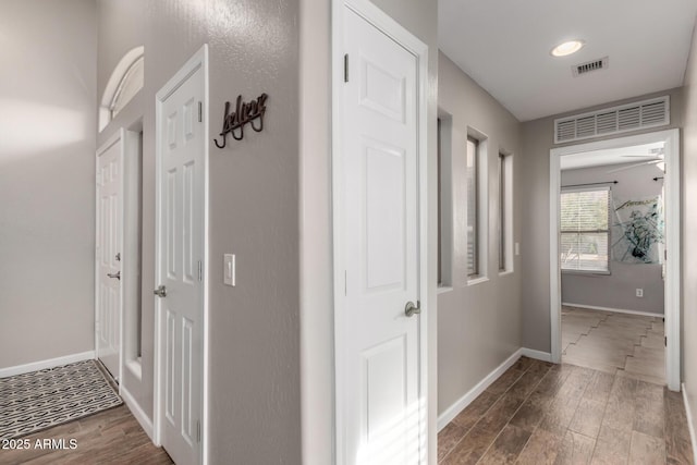 hallway with baseboards, visible vents, and wood finished floors