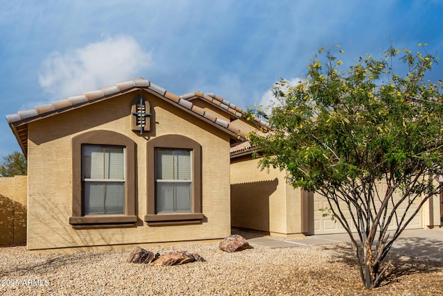 view of home's exterior featuring a tiled roof, an attached garage, driveway, and stucco siding