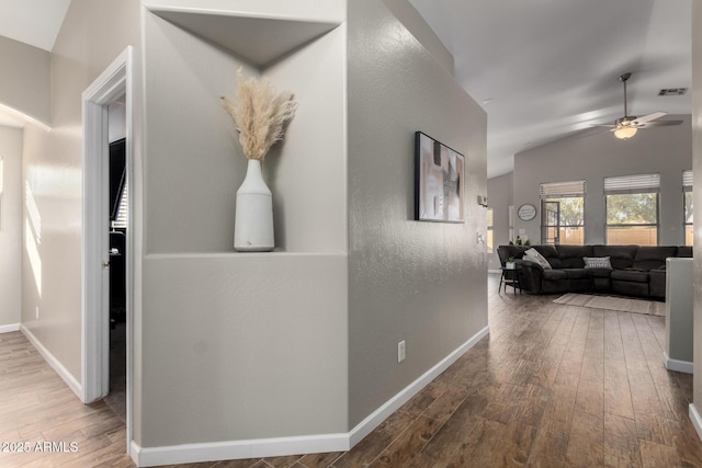 hallway featuring lofted ceiling, wood-type flooring, visible vents, and baseboards