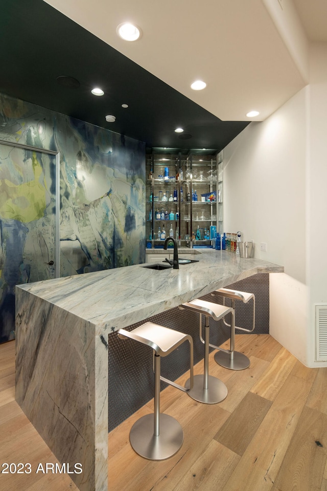 bar featuring light hardwood / wood-style floors, sink, and light stone counters