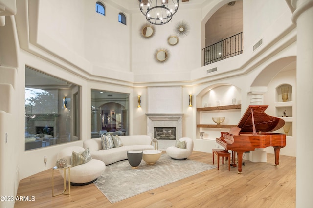 living room featuring built in features, a chandelier, a towering ceiling, and light hardwood / wood-style flooring