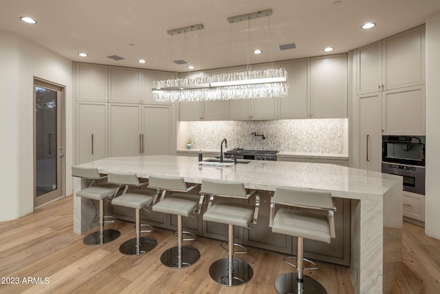 kitchen with a kitchen breakfast bar, a kitchen island with sink, light stone countertops, and pendant lighting