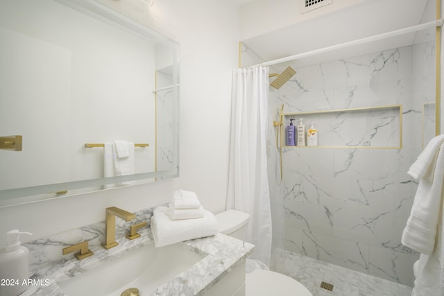 bathroom with toilet, a marble finish shower, and vanity