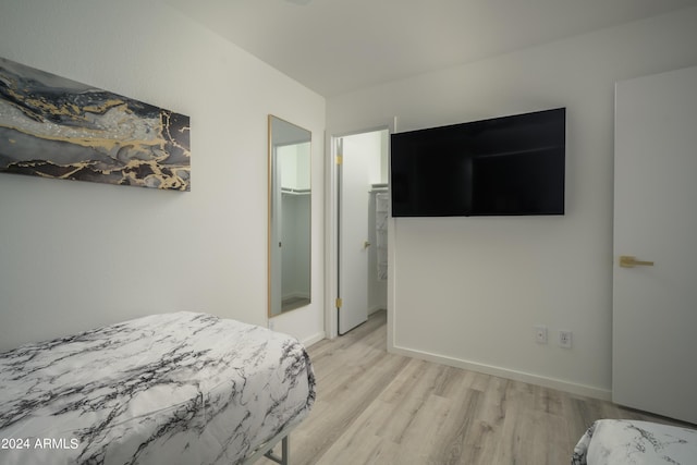 bedroom featuring a spacious closet, a closet, light wood-type flooring, and baseboards