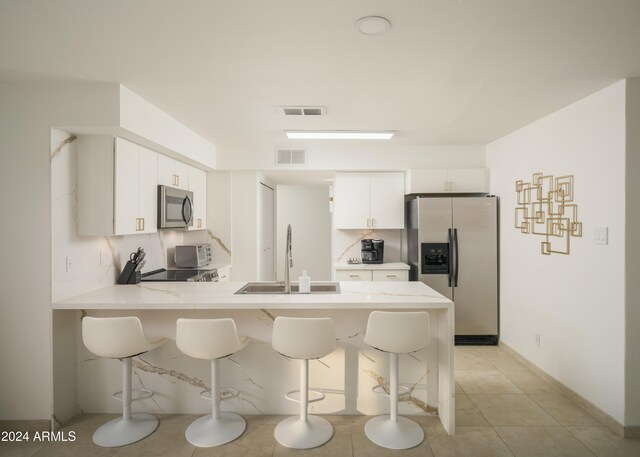 kitchen featuring a breakfast bar area, kitchen peninsula, white cabinets, appliances with stainless steel finishes, and sink