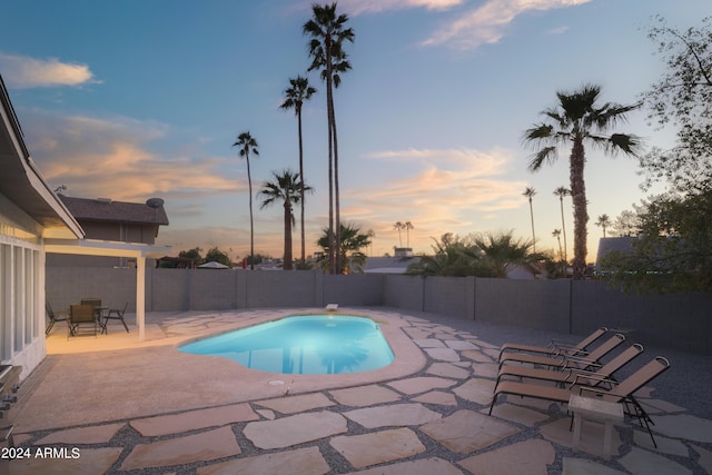 pool at dusk featuring a patio area, a fenced backyard, and a fenced in pool