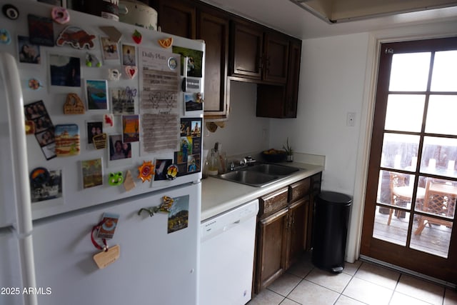 kitchen with a sink, white appliances, dark brown cabinetry, light countertops, and light tile patterned floors