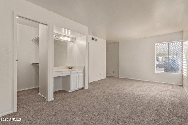 unfurnished bedroom with connected bathroom, sink, a spacious closet, built in desk, and light colored carpet