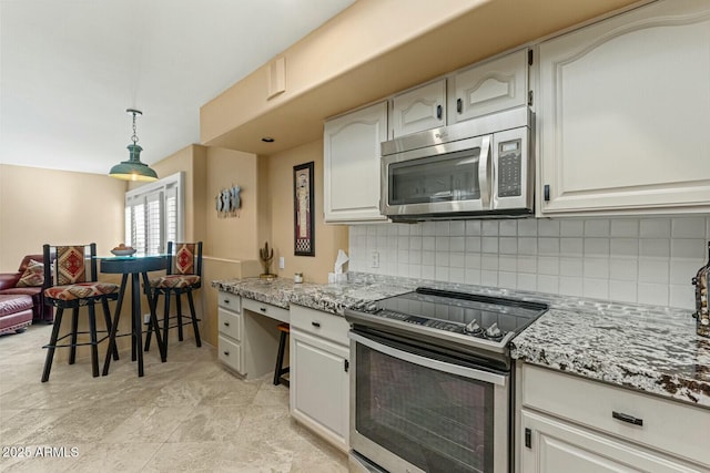 kitchen with appliances with stainless steel finishes, white cabinetry, hanging light fixtures, light stone countertops, and decorative backsplash