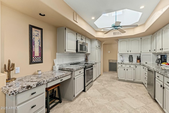 kitchen featuring stainless steel appliances, a tray ceiling, decorative backsplash, and a skylight