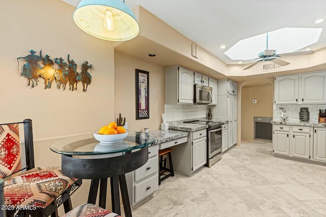 kitchen featuring tasteful backsplash, a skylight, stainless steel appliances, and light stone countertops