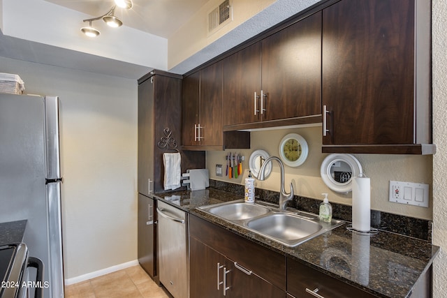 kitchen with appliances with stainless steel finishes, sink, dark brown cabinets, light tile patterned floors, and dark stone countertops