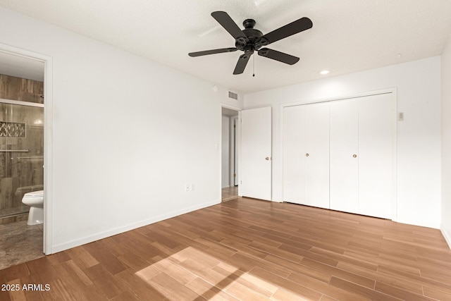 unfurnished bedroom featuring ceiling fan, a closet, connected bathroom, and wood-type flooring