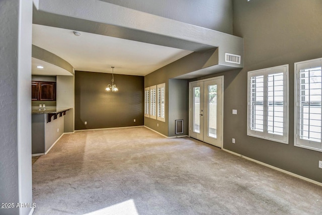 unfurnished living room featuring a notable chandelier, carpet floors, visible vents, baseboards, and french doors