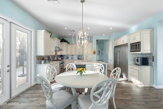 kitchen with dark wood-type flooring, hanging light fixtures, built in appliances, a notable chandelier, and light stone countertops