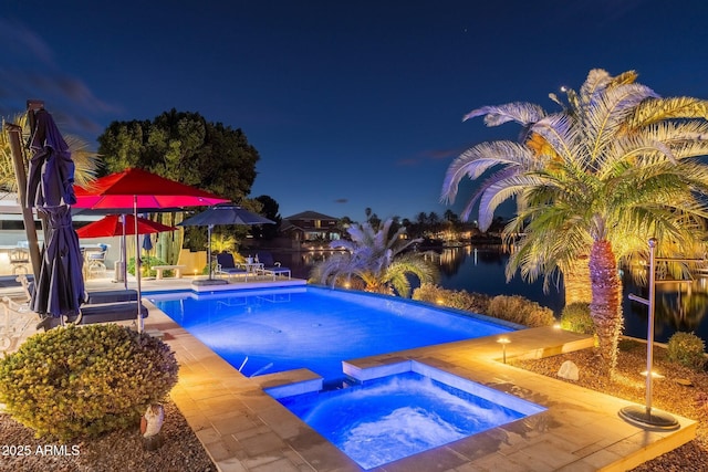 pool at night featuring an in ground hot tub and a water view