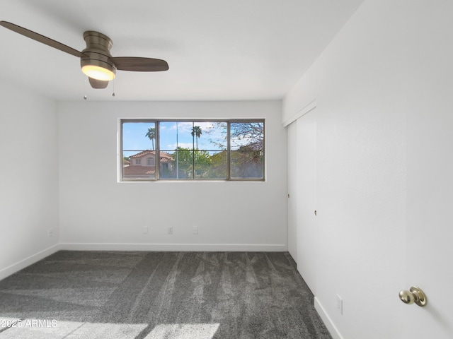 empty room featuring baseboards, a ceiling fan, and dark carpet