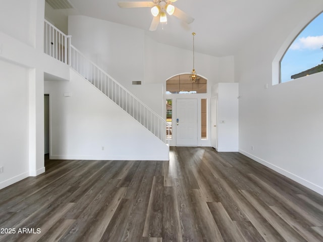 unfurnished living room with stairs, a high ceiling, wood finished floors, and baseboards