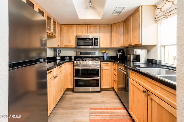 5209 N 78th St, Scottsdale, AZ 85250 - kitchen featuring stainless steel appliances, light wood-style floors, light brown cabinets, dark countertops, and glass insert cabinets