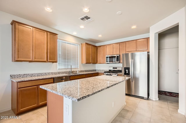 kitchen featuring light stone countertops, stainless steel appliances, sink, light tile patterned floors, and a kitchen island