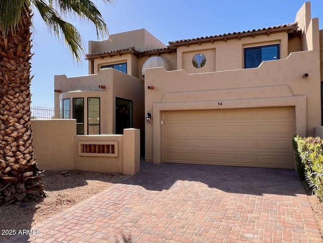 view of front facade featuring decorative driveway, fence, an attached garage, and stucco siding