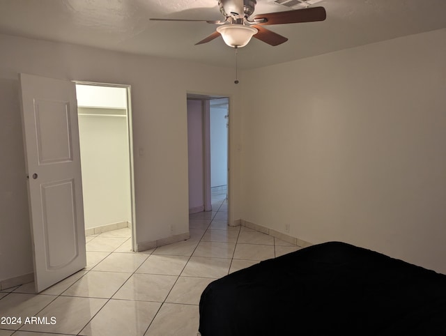 unfurnished bedroom with ceiling fan, a walk in closet, light tile floors, and a closet