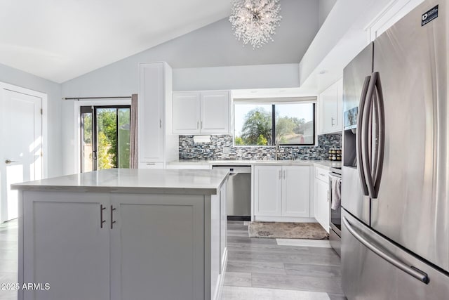 kitchen with lofted ceiling, appliances with stainless steel finishes, light stone counters, white cabinets, and a kitchen island