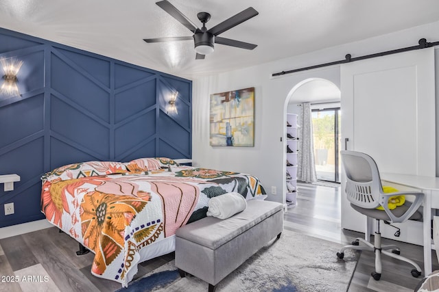 bedroom featuring hardwood / wood-style flooring, a barn door, and ceiling fan