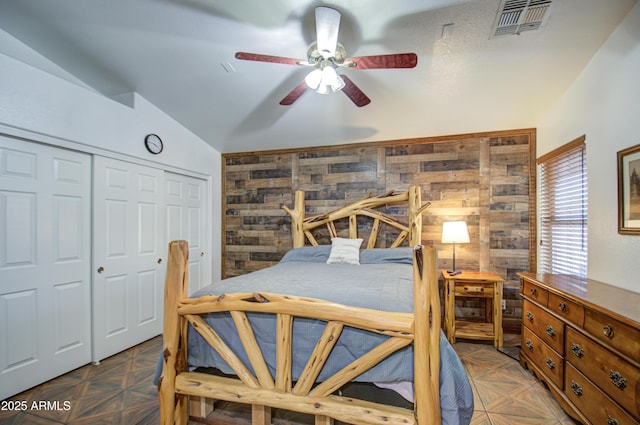 bedroom with ceiling fan, wooden walls, parquet floors, vaulted ceiling, and a closet