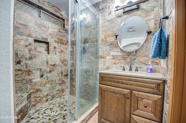 bathroom featuring a shower with door, vanity, and tile walls