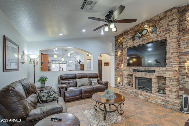 living room with parquet flooring, ceiling fan, a stone fireplace, and a textured ceiling