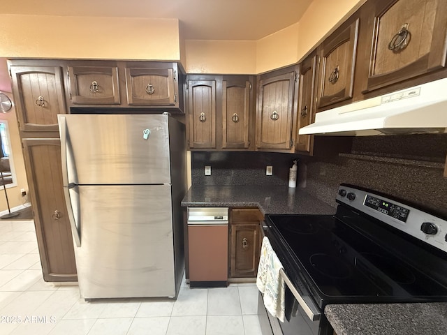 kitchen with under cabinet range hood, backsplash, dark countertops, appliances with stainless steel finishes, and light tile patterned floors