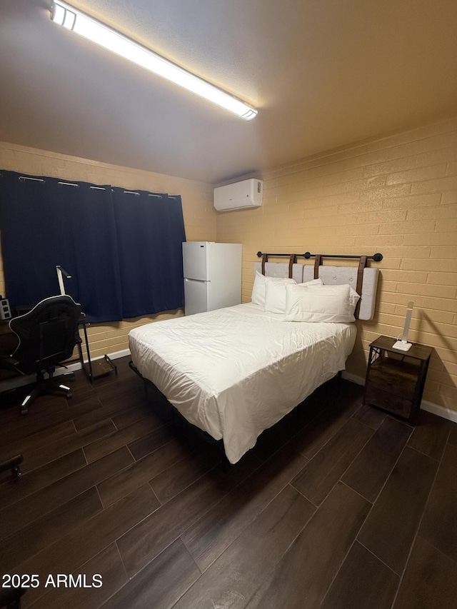 bedroom featuring wood finish floors, a wall mounted air conditioner, brick wall, and freestanding refrigerator