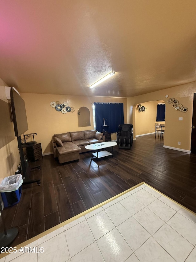 living area featuring arched walkways, a textured ceiling, baseboards, and wood finished floors