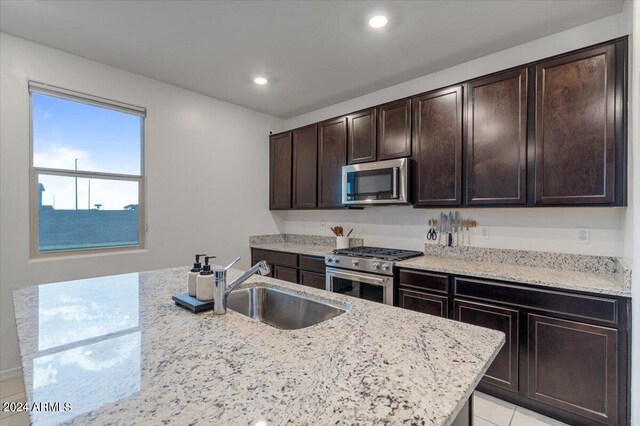 kitchen featuring light stone countertops, dark brown cabinets, light tile patterned floors, stainless steel appliances, and sink