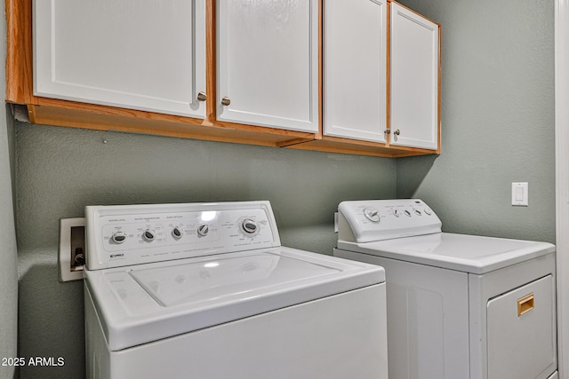 washroom featuring a textured wall, washer and clothes dryer, and cabinet space