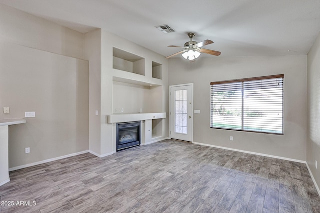 unfurnished living room with baseboards, visible vents, a ceiling fan, a glass covered fireplace, and light wood-type flooring