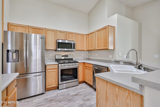 kitchen with light countertops, a towering ceiling, appliances with stainless steel finishes, light brown cabinets, and a sink