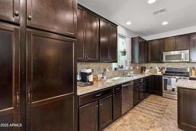 kitchen with sink, dark brown cabinets, stainless steel appliances, light stone counters, and decorative backsplash