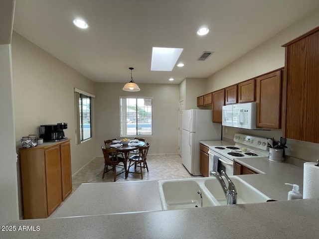 kitchen with brown cabinets, white appliances, light countertops, a skylight, and visible vents