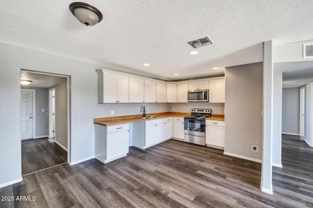 kitchen with dark wood finished floors, stainless steel appliances, visible vents, a sink, and wood counters