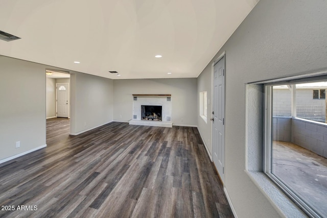 unfurnished living room featuring dark wood-style flooring, recessed lighting, a fireplace with raised hearth, visible vents, and baseboards