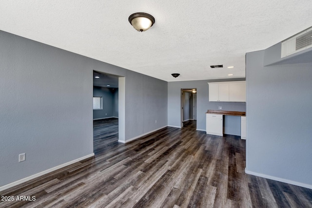 unfurnished living room featuring dark wood-type flooring, visible vents, built in desk, and baseboards