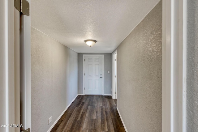 hall with dark wood-style flooring, a textured wall, a textured ceiling, and baseboards