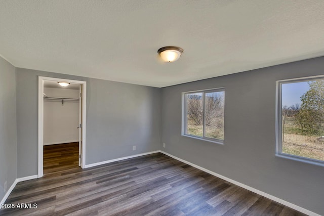 unfurnished bedroom with a closet, a walk in closet, dark wood-style flooring, and baseboards