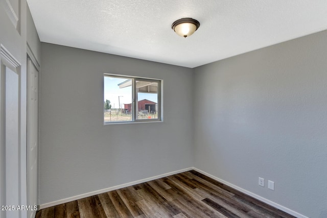 empty room featuring baseboards, dark wood finished floors, and a textured ceiling